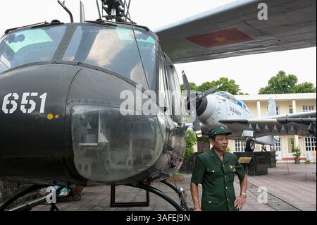 VIETNAM, Hanoi, Militärmuseum, Militärausrüstung und Kriegsschrott aus dem französischen Kolonialkrieg 1946-1954 und dem US-amerikanischen Krieg in Vietnam 1955–1975, vietnamesischer Kriegsveteran am US-Hubschrauber Iroquois UH-1H / VIETNAM, Hanoi, Militärmuseum, Ausstellung mit Waffen zum Krieg der Amerikaner in Vietnam, Vietnamesischer Kriegsveteran posiert an einem US Helikopter Stockfoto