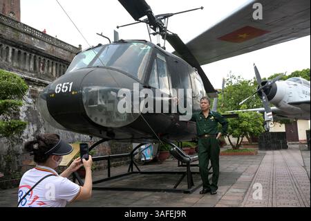 VIETNAM, Hanoi, Militärmuseum, Militärausrüstung und Kriegsschrott aus dem französischen Kolonialkrieg 1946-1954 und dem US-amerikanischen Krieg in Vietnam 1955–1975, vietnamesischer Kriegsveteran am US-Hubschrauber Iroquois UH-1H / VIETNAM, Hanoi, Militärmuseum, Ausstellung mit Waffen zum Krieg der Amerikaner in Vietnam, Vietnamesischer Kriegsveteran posiert an einem US Helikopter Stockfoto
