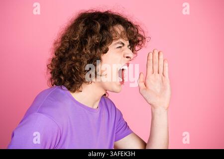 Porträt eines jungen Mannes, der mit einer Handgeste auf rosa Hintergrund brüllt Stockfoto