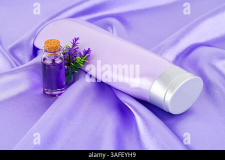 Die Flasche mit Kosmetikprodukten und Blumen auf dem lilafarbenen Seidenhintergrund. Stockfoto