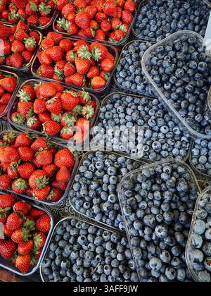 Beeren zum Verkauf auf dem Bauernmarkt. Transparente Kunststoffschalen mit frischen bunten Heidelbeeren oder Heidelbeeren und Erdbeeren. Stockfoto