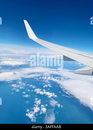 Fliegen über dem Meer - Blick auf den Fenstersitz. Weißer Flugzeugflügel gegen blauen Himmel in 10 000 Metern Höhe. Stockfoto
