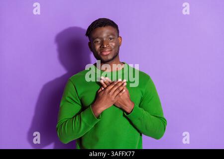 Junger Mann mit grünem Sweatshirt, der Dankbarkeit mit Händen über dem Herzen vor einem leuchtend violetten Hintergrund ausdrückt Stockfoto