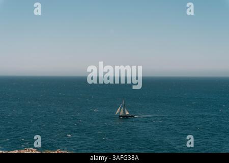 Ein einsames Segelboot gleitet über das tiefblaue Wasser von Sagres und verkörpert Gelassenheit und maritimes Abenteuer, während der Atlantik sich endlos über den Horizont erstreckt Stockfoto