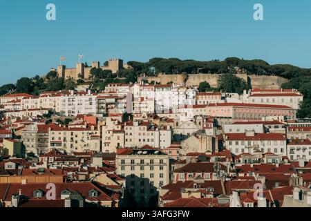 Die Golden Hour strahlt ein warmes Leuchten über Lissabons historisches Schloss São Jorge und die Skyline mit roten Dächern aus und bietet zeitlosen Charme und malerische Schönheit Stockfoto