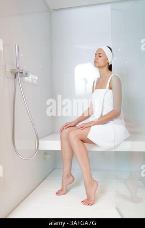 Frau im Handtuch, die sich in der modernen Dampfduschkabine entspannt, Spa-Therapie und Wellness-Behandlung allein genießt. Stockfoto