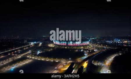 Eine Drohne fängt Warschaus leuchtende Skyline bei Nacht ein: PGE Narodowy, Świętokrzyski-Brücke und endlose Lichter der Stadt, die sich auf dem Fluss Wisła spiegeln. Stockfoto