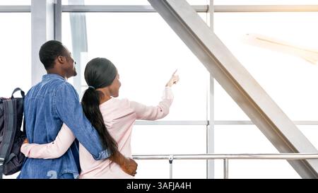 Aufgeregtes afrikanisches Paar, das den Abflug vom Fenster am Flughafen ansah Stockfoto
