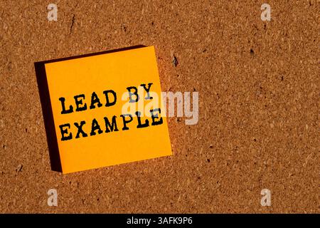 Beispiel-Meldung auf orangefarbenem Papier auf braunem Hintergrund. Konzeptuelle Führung durch Beispielsymbol. Kopierbereich. Stockfoto