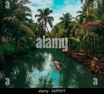 Blick aus der Vogelperspektive auf einen ruhigen Fluss, umgeben von üppigen Palmen auf Siargao Island, Philippinen, mit einem kleinen Boot mit zwei Personen Stockfoto