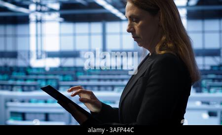 Akribischer Techniker, der die Überprüfung durchführt und Daten auf ein Tablet mit erforderlichen Fixes im Server-Hub eingibt, in dem eine erweiterte Datenspeicherinfrastruktur zur Unterstützung kritischer IT-Workloads, Kamera A, untergebracht ist Stockfoto