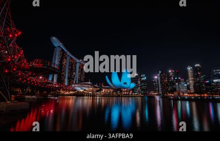 Beleuchtete Nachtlandschaft von Marina Bay Sands und Helix Bridge in Singapur, die sich wunderbar auf dem ruhigen Wasser unter einem Sternenhimmel spiegelt Stockfoto