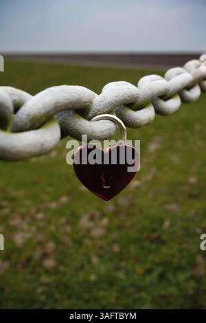 Eine herzförmige Burg, die an einer schweren Kette hängt, mit einem grünen Deich im Hintergrund, Nordseestrand 26316 Varel Dangast-Deutschland Stockfoto