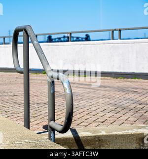 Treppengeländer aus Metall, die durch weiße Betonwand in einen gepflasterten Bereich führen Stockfoto