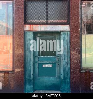 Teal-Metalltür mit geometrischen Fensterdetails an einer verwitterten Gebäudefassade in Chicago, mit Rostflecken und Reflexen des urbanen Straßenlebens Stockfoto