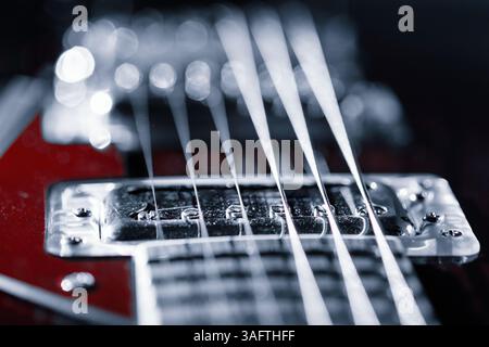 Die Gitarrenbrücke zeigt glänzendes Metall und straffe Saiten vor einem schlanken, roten Körper und erfasst komplizierte Details. Unscharfer Hintergrund mit Bokeh-Lichtern Stockfoto