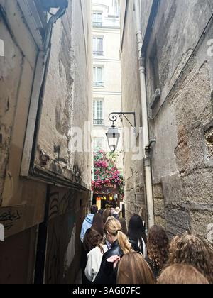 Paris, Frankreich - 28. März 2025: Gruppe von Menschen, die durch die enge Pariser Straße mit lebhaften Blumen und Gebäuden spazieren gehen Stockfoto