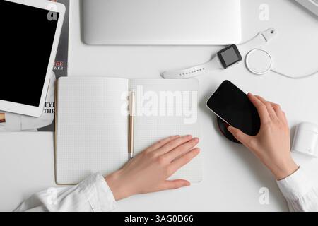 Weibliche Hände mit modernen Gadgets, Notizbuch und Stift auf hellem Hintergrund Stockfoto