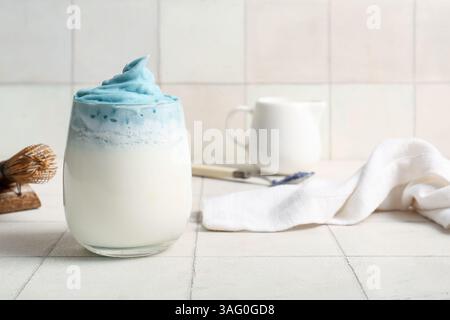 Glas blauer Dalgona Matcha Latte, Kanne und Serviette auf dem Tisch Stockfoto