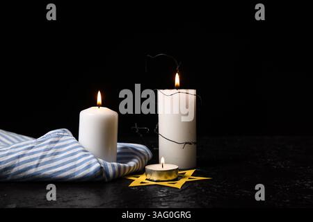 Gefangenenuniform, brennende Kerzen und David-Stern auf dunklem Hintergrund. Holocaust-Gedenktag Stockfoto