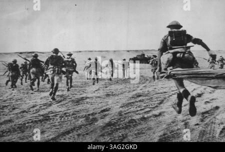 Sturming A Ridge im Wüstenkrieg - die britische Infanterie steigt im libyschen Wüstenkrieg auf den Doppel-Rücken in Richtung Ridge vor, in dem Rommels Männer gerutscht wurden. Panzer im Hintergrund ist ein Achsenfahrzeug, das bei ihrem Gegenangriff, der diesem britischen Angriff vorausging, deaktiviert wurde. November 1942. (Foto von AP Wirephoto). Stockfoto