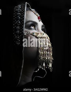 Porträt einer Frau in traditioneller nahöstlicher Kleidung mit verziertem Gesichtsschleier und Kopfschmuck, aufgenommen in dramatischer Beleuchtung Stockfoto