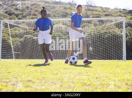 Auf dem Schulfeld Fußball spielen zwei verschiedene Mädchen in Sportuniformen, die das Spiel genießen Stockfoto