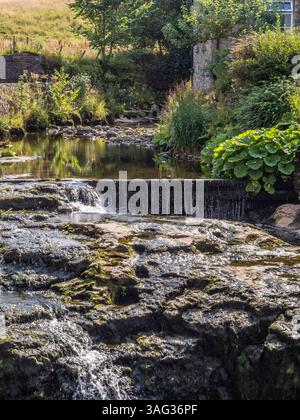 Gayle Beck mit einem kleinen Wasserfall, der neben einem Steinhaus an einem sonnigen Sommertag in Hawes, Yorkshire Dales fließt. Stockfoto