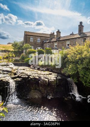 Gayle Beck mit einem kleinen Wasserfall, der neben einem Steinhaus an einem sonnigen Sommertag in Hawes, Yorkshire Dales fließt. Stockfoto