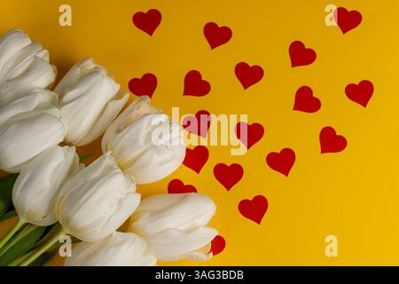 Frische und schöne weiße Tulpen auf gelbem Papier mit roten Herzen, roten Herzen und weißen Tulpenblüten auf Papier Stockfoto
