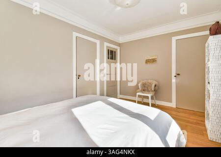 Ein gut beleuchtetes, minimalistisches Schlafzimmer mit weicher weißer Bettwäsche und Naturholzfußboden. Die Wände sind in neutralen Tönen gestrichen und sorgen für ein beruhigendes Ambiente. Stockfoto