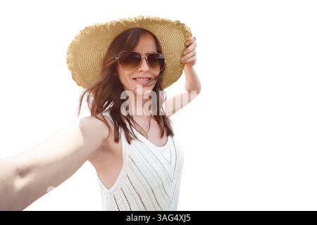 Eine fröhliche junge Frau macht ein freudiges Selfie im Freien, stolz mit einem stilvollen Sonnenhut und einer modischen Sonnenbrille, Porträt einer Reisenden blo Stockfoto