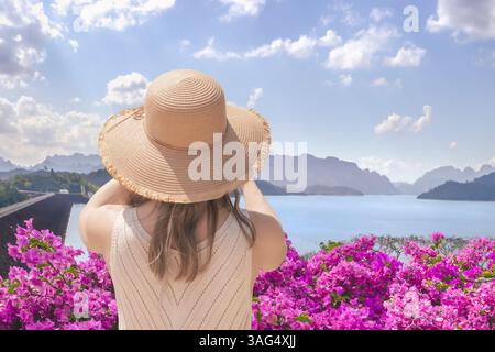 Eine Touristenfrau mit breiter Krempe fotografiert den Lake Checo Lan und den Damm von einem Aussichtspunkt aus, von hinten. Thailändische Touristenattraktionen wie Stockfoto