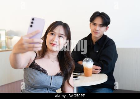 Junges glückliches asiatisches Paar, das im Café sitzt und sich drinnen mit Selfie verabredet Stockfoto