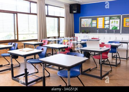 Leeres Klassenzimmer mit Schreibtischen und Stühlen, Laptop auf einem Schreibtisch, helle Fenster, Kopierraum Stockfoto