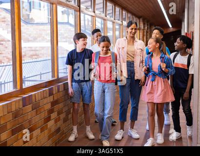 Im Schulflur spazieren, indische Lehrerin und Schüler lächeln und reden miteinander Stockfoto