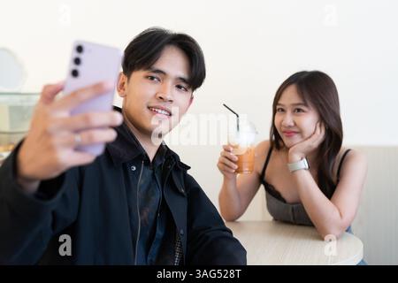 Junges glückliches asiatisches Paar, das im Café sitzt und sich drinnen mit Selfie verabredet Stockfoto