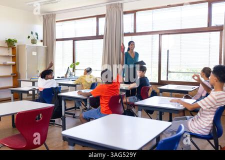 In der Schule hielt eine indische Lehrerin ein Tablett und die Schülerinnen heben im Klassenzimmer die Hände Stockfoto