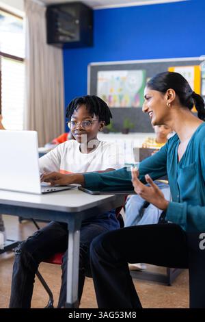 In der Schule hilft eine indische Lehrerin der Schülerin mit einem Laptop im Klassenzimmer und spricht über den Unterricht Stockfoto