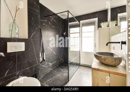 Ein stilvolles, modernes Badezimmer mit Glasdusche, dunklen Marmorwänden und Tageslicht durch große Fenster. Elegant und funktional. Stockfoto