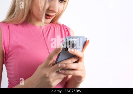 Nahaufnahme eines blonden kaukasischen Mädchens in ärmellosem rosa Hemd mit ihrem Smartphone. Chatten, Messaging, Scrollen, Surfen, soziale Medien, Schönheit. Stockfoto