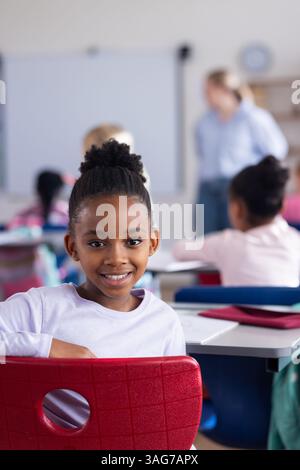 In der Schule lächelte ein afroamerikanisches Mädchen am Schreibtisch im Klassenzimmer und sah glücklich aus Stockfoto