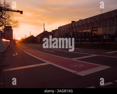 Sonnenuntergang über einer ruhigen Stadtstraße mit Radweg und Bahnhof, Karlsruhe (Deutschland) Stockfoto