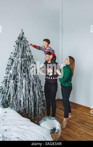 In einem gemütlichen Wohnzimmer versammelt sich eine fröhliche Familie, um ihren Weihnachtsbaum zu dekorieren und den Zauber der Weihnachtszeit mit Spannung zu genießen und zu feiern Stockfoto