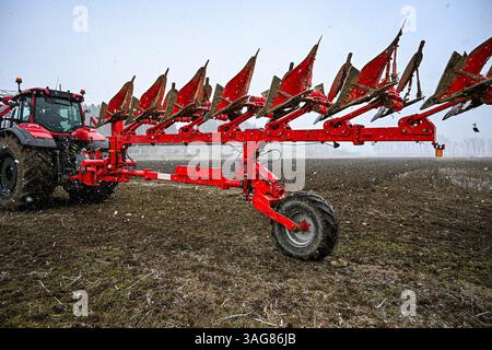 Roter Traktor zieht Pflug durch verschneite Felder und bereitet Boden für die Pflanzung während der Wintersaison vor. Stockfoto