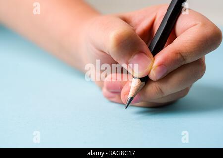 Die linke Hand hält einen Kugelschreiber auf einem offenen Notizbuch auf blauem Hintergrund Stockfoto