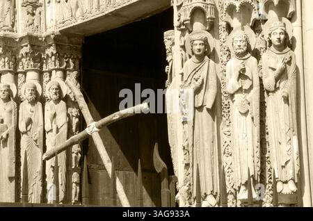 Kreuz und Eingang zur Kathedrale von Chartres im Hintergrund. Selektive Fokussierung auf die Figuren der Heiligen. Chartres, Frankreich. Historisches Foto von Sepia Stockfoto