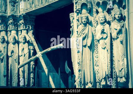 Kreuz und Eingang zur Kathedrale von Chartres (Frankreich) im Hintergrund. Selektive Fokussierung auf die Figuren der Heiligen. Retro-Foto im Alter. Stockfoto