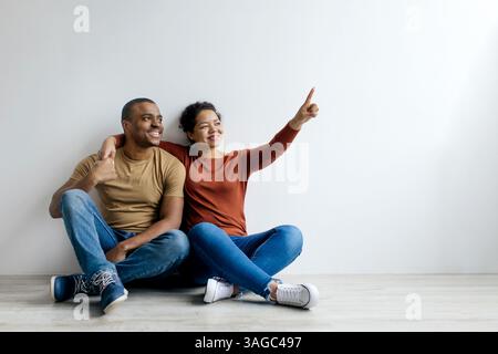 Ein junges schwarzes Paar, das sich umschließt und nach oben zeigt, während er auf dem Boden sitzt Stockfoto