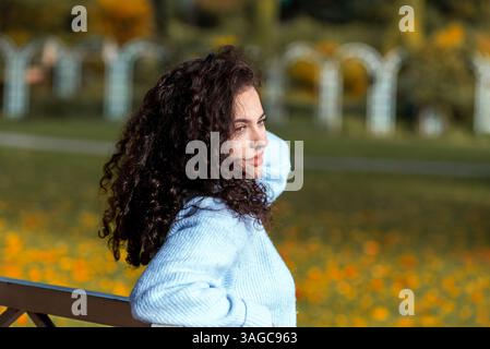 Millennial Frau mit schönen lockigen Haaren Seitenansicht Porträt an einem sonnigen Herbsttag in einem öffentlichen Park Stockfoto